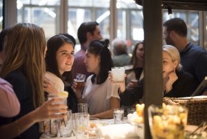 Women smiles among crowd with cocktail in hand while sitting at the bar of Spainish restaurant, Boqueria.