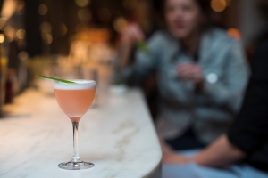 ALMA DEL SUR, A light pink drink made with El Gobernador Pisco, Giffard ‘Pineapple’, Lime, Peychaud’s, and egg white, topped with a garnish of pineapple leaf and served in a nick and nora glass.